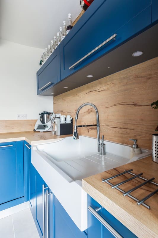 Cuisine en L blanche bois et bleue avec îlot central avec cave à Caulnes | Raison Home - 5