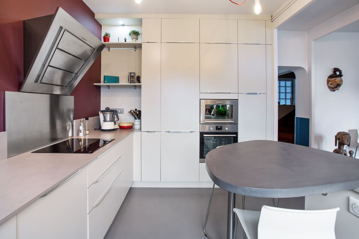 Cuisine blanche avec table en triangle avec un mur bordeau à Tours | Raison Home - 3