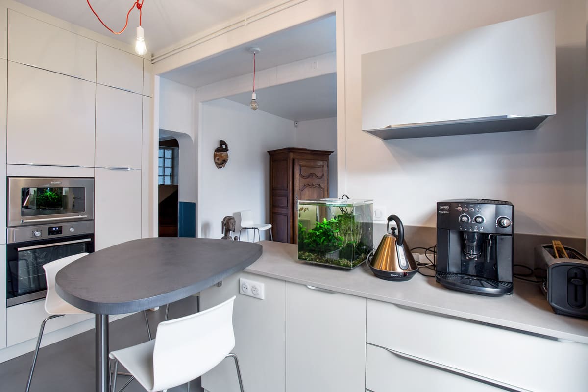 Cuisine blanche avec table en triangle avec un mur bordeau à Tours | Raison Home - 2