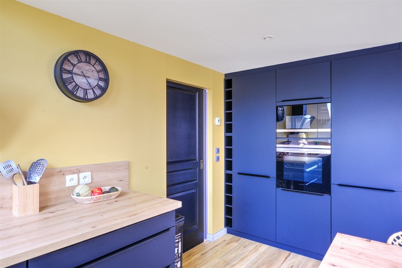 Cuisine ouverte bleu et bois avec mur jaune à Cuverville | Raison Home - 3